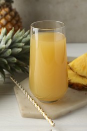 Photo of Tasty pineapple juice in glass and fresh fruits on white wooden table against grey background, closeup