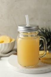 Photo of Tasty pineapple juice in mason jar and fresh fruits on white wooden table against grey background, closeup