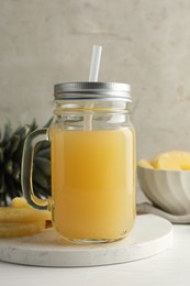 Photo of Tasty pineapple juice in mason jar and fresh fruits on white wooden table against grey background, closeup