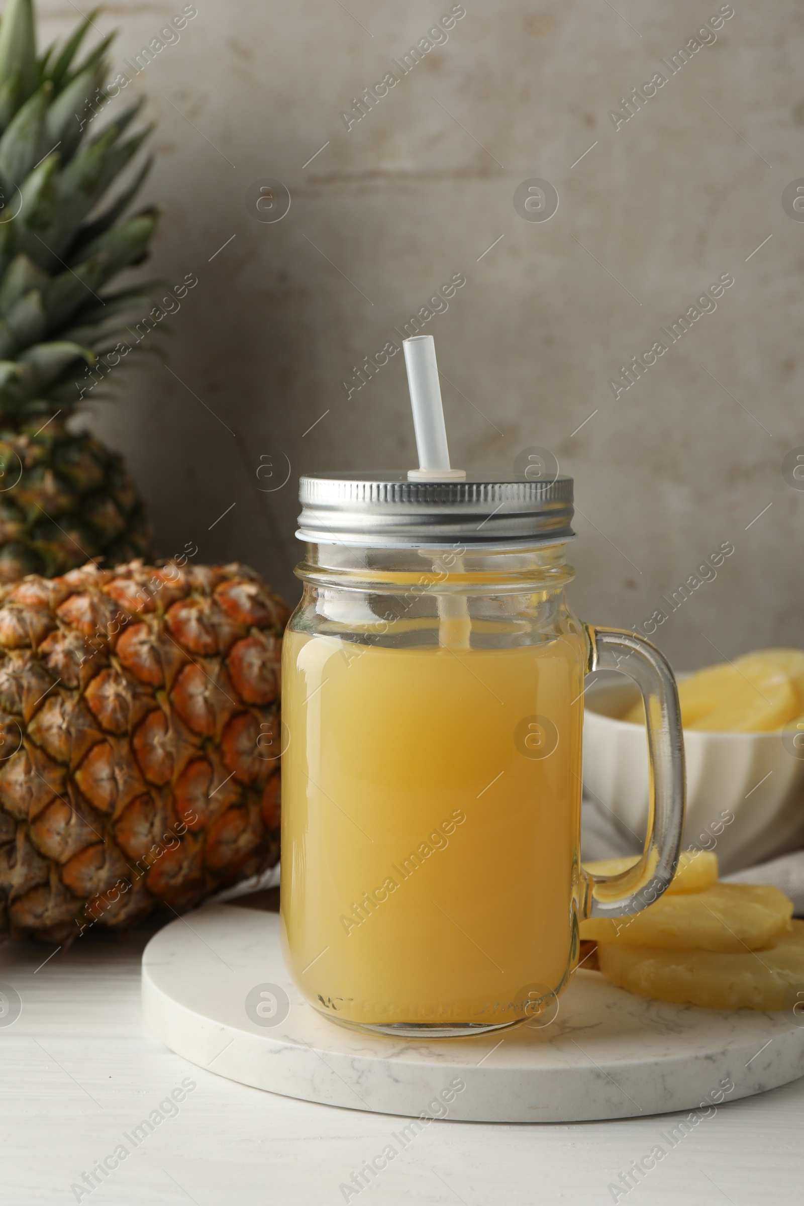 Photo of Tasty pineapple juice in mason jar and fresh fruits on white wooden table against grey background