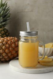 Photo of Tasty pineapple juice in mason jar and fresh fruits on white wooden table against grey background