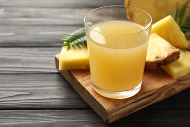 Photo of Tasty pineapple juice in glass and slices of fresh fruit on wooden table, closeup. Space for text