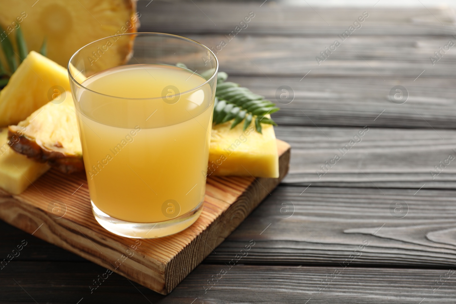 Photo of Tasty pineapple juice in glass and slices of fresh fruit on wooden table, closeup. Space for text