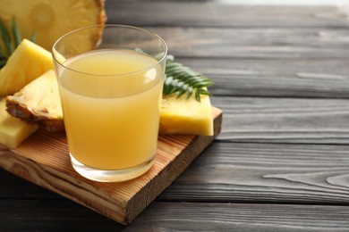 Photo of Tasty pineapple juice in glass and slices of fresh fruit on wooden table, closeup. Space for text