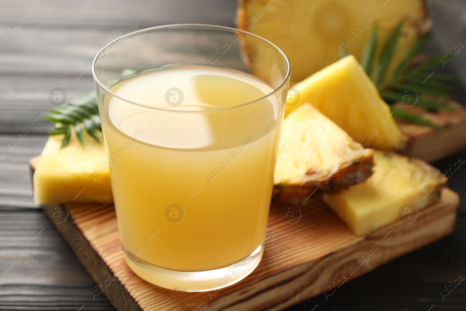 Photo of Tasty pineapple juice in glass and slices of fresh fruit on wooden table, closeup