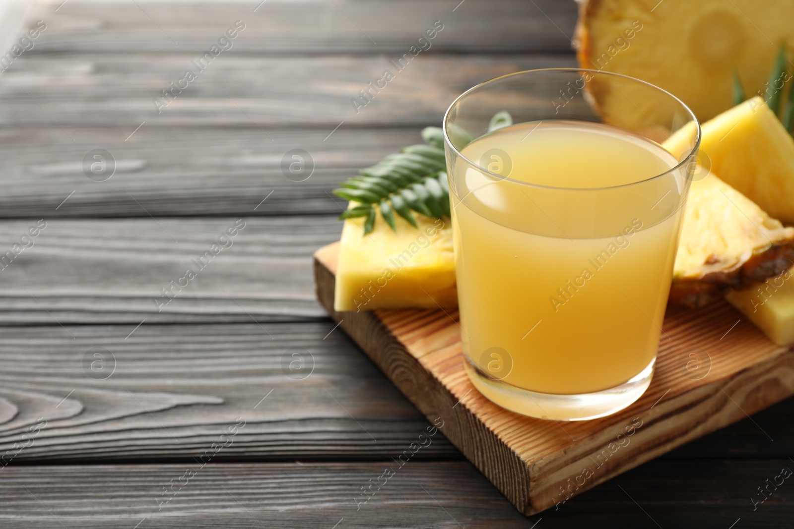 Photo of Tasty pineapple juice in glass and slices of fresh fruit on wooden table, closeup. Space for text