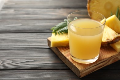 Photo of Tasty pineapple juice in glass and slices of fresh fruit on wooden table, closeup. Space for text