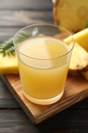 Photo of Tasty pineapple juice in glass and slices of fresh fruit on wooden table, closeup