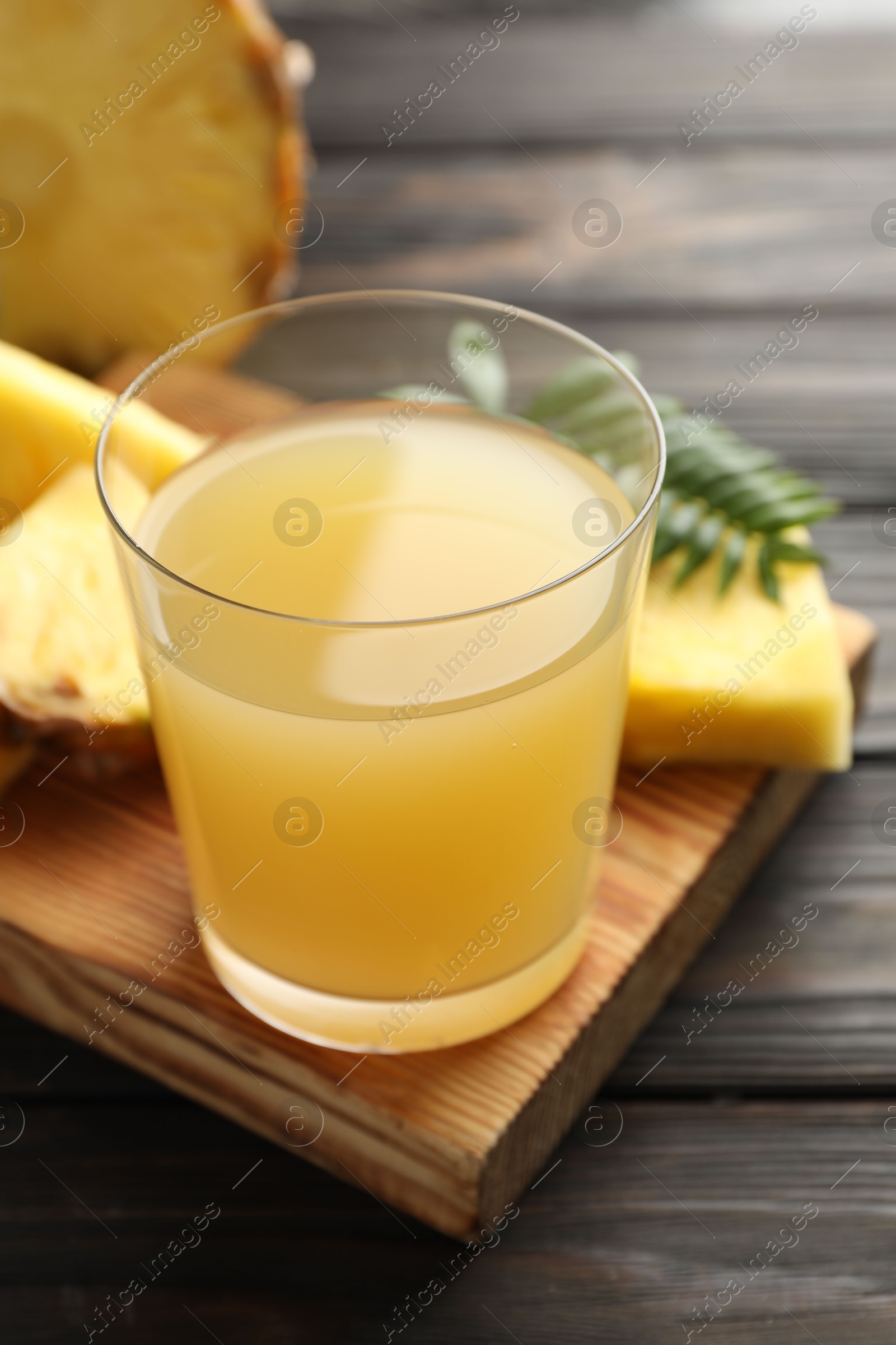 Photo of Tasty pineapple juice in glass and slices of fresh fruit on wooden table, closeup