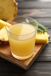 Photo of Tasty pineapple juice in glass and slices of fresh fruit on wooden table, closeup