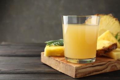 Photo of Tasty pineapple juice in glass and slices of fresh fruit on wooden table, closeup. Space for text