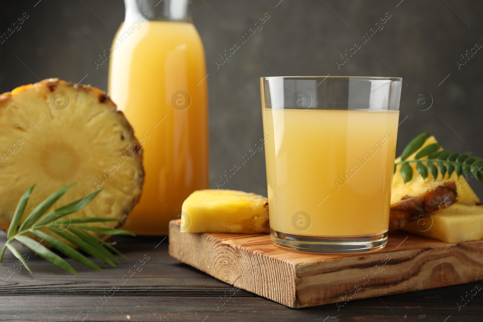 Photo of Tasty pineapple juice in glass and slices of fresh fruit on wooden table, closeup