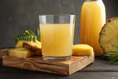 Photo of Tasty pineapple juice in glass and slices of fresh fruit on wooden table, closeup