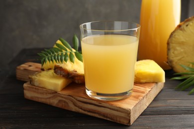 Photo of Tasty pineapple juice in glass and slices of fresh fruit on wooden table, closeup