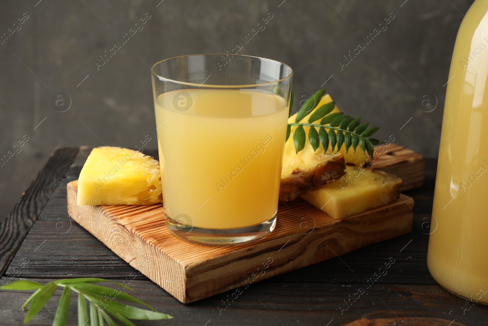 Photo of Tasty pineapple juice in glass and slices of fresh fruit on wooden table, closeup