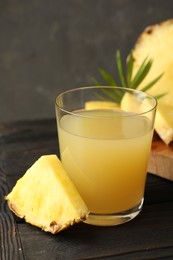 Photo of Tasty pineapple juice in glass and slice of fresh fruit on wooden table, closeup