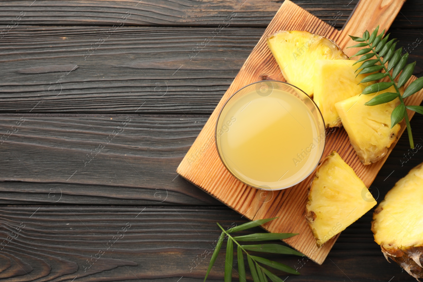 Photo of Tasty pineapple juice in glass and slice of fresh fruit on wooden table, flat lay. Space for text