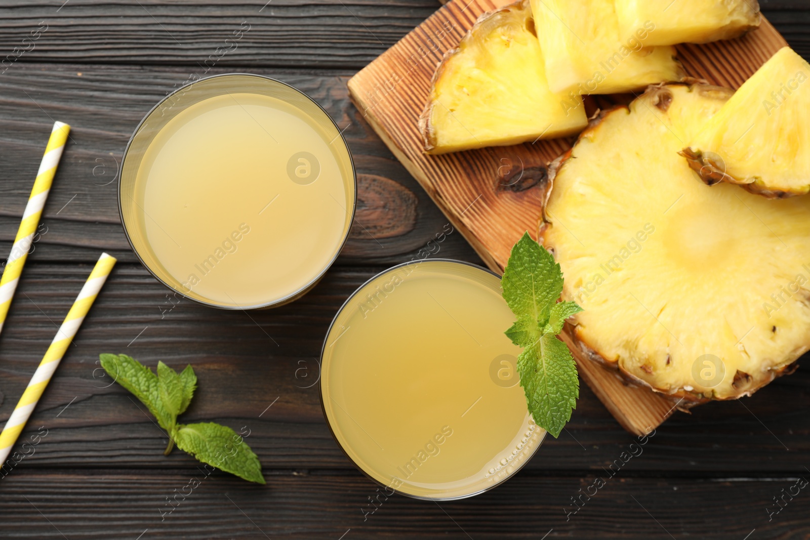 Photo of Tasty pineapple juice in glasses, mint and slice of fresh fruit on wooden table, flat lay