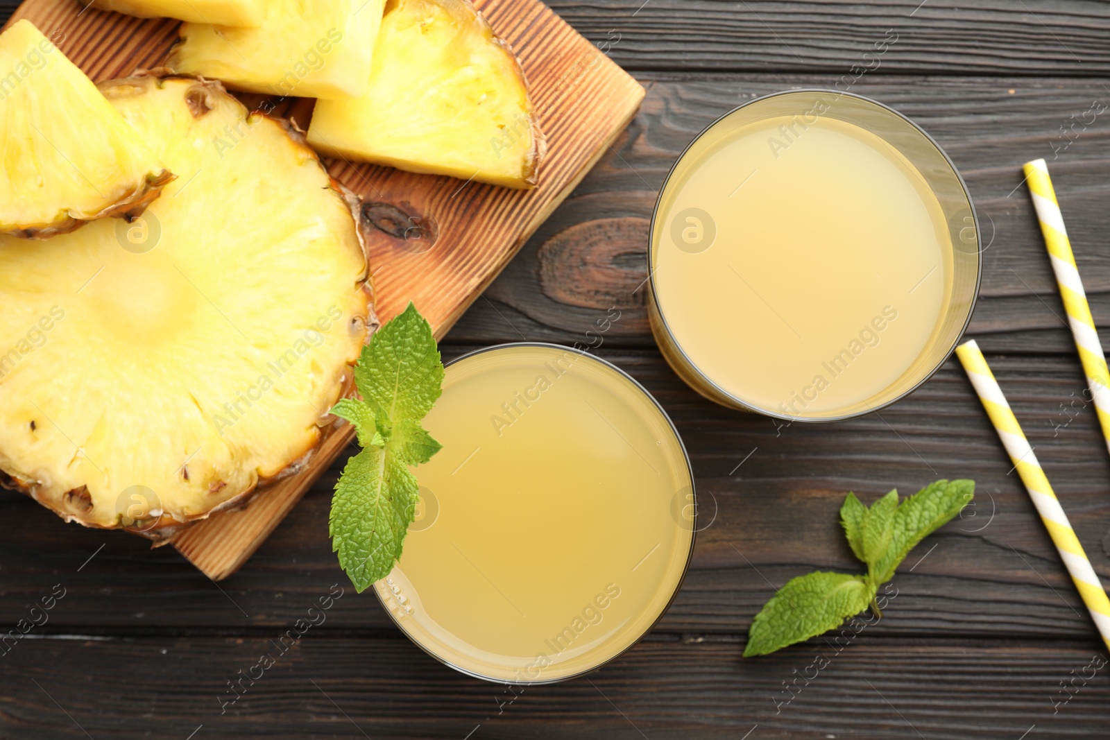 Photo of Tasty pineapple juice in glasses, mint and slice of fresh fruit on wooden table, flat lay