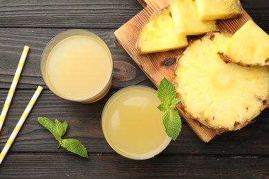 Photo of Tasty pineapple juice in glasses, mint and slice of fresh fruit on wooden table, flat lay