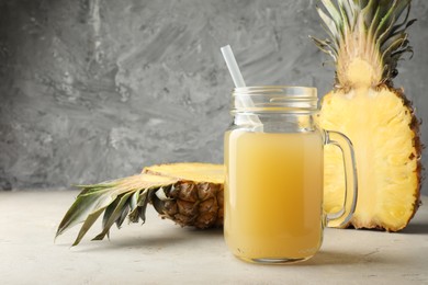 Photo of Tasty pineapple juice in mason jar and halves of fresh fruit on grey textured table, closeup. Space for text