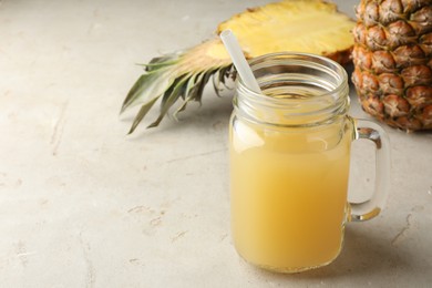 Photo of Tasty pineapple juice in mason jar and fresh fruits on grey textured table, closeup. Space for text