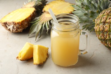 Photo of Tasty pineapple juice in mason jar and fresh fruits on grey textured table, closeup