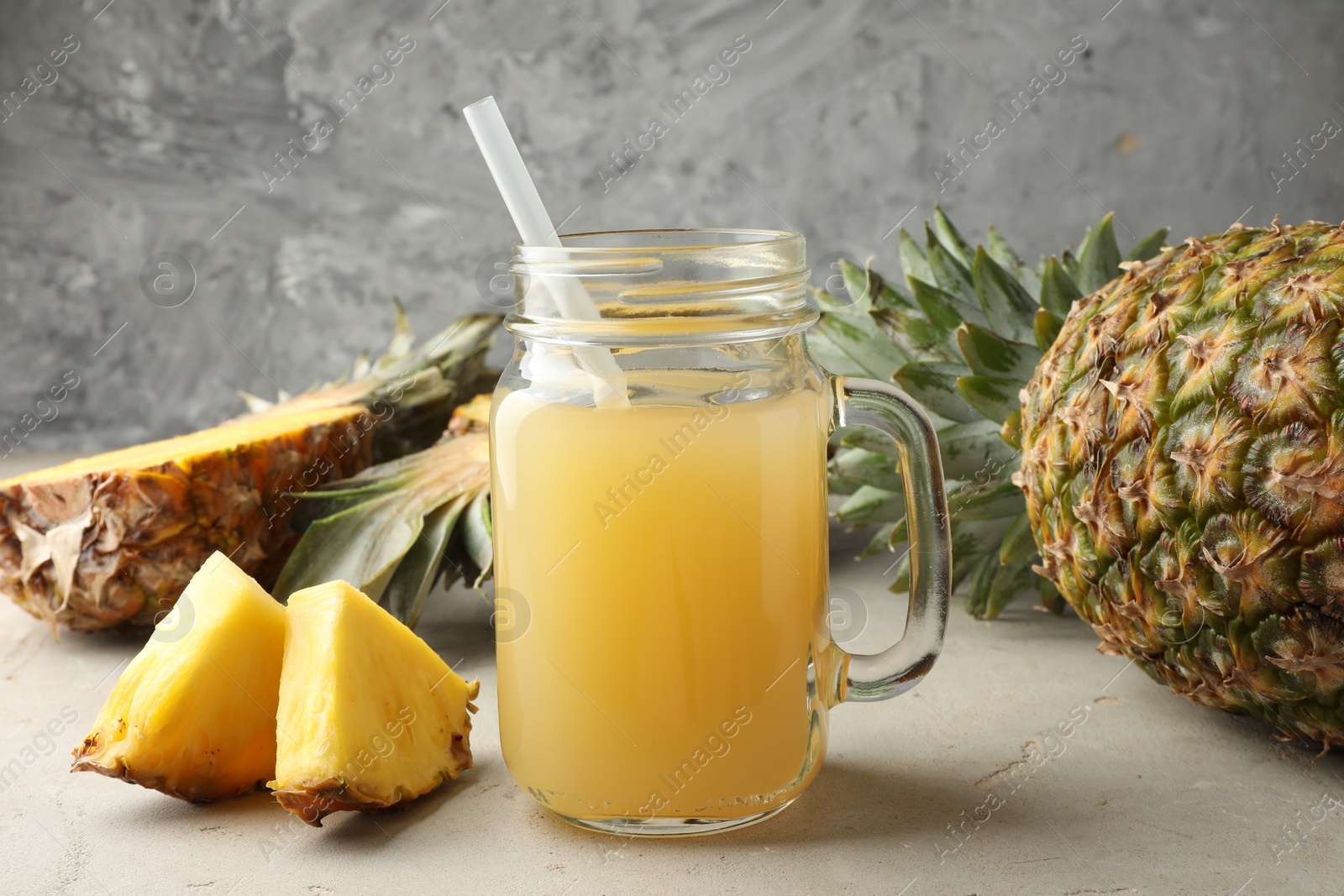 Photo of Tasty pineapple juice in mason jar and fresh fruits on grey textured table, closeup