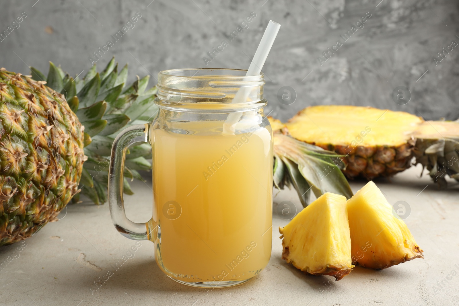 Photo of Tasty pineapple juice in mason jar and fresh fruits on grey textured table, closeup