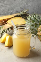 Photo of Tasty pineapple juice in mason jar and fresh fruits on grey textured table, closeup