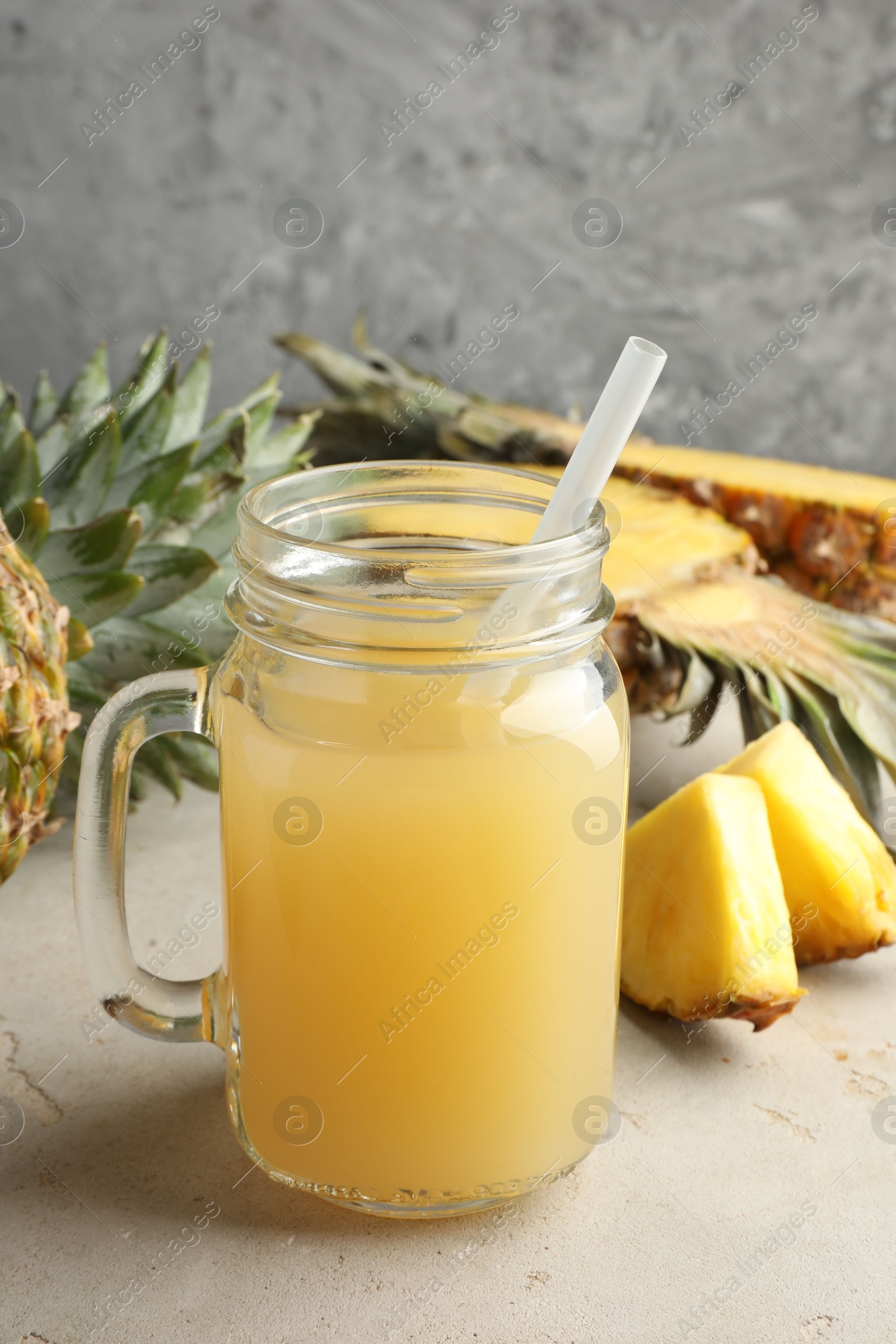 Photo of Tasty pineapple juice in mason jar and fresh fruits on grey textured table, closeup