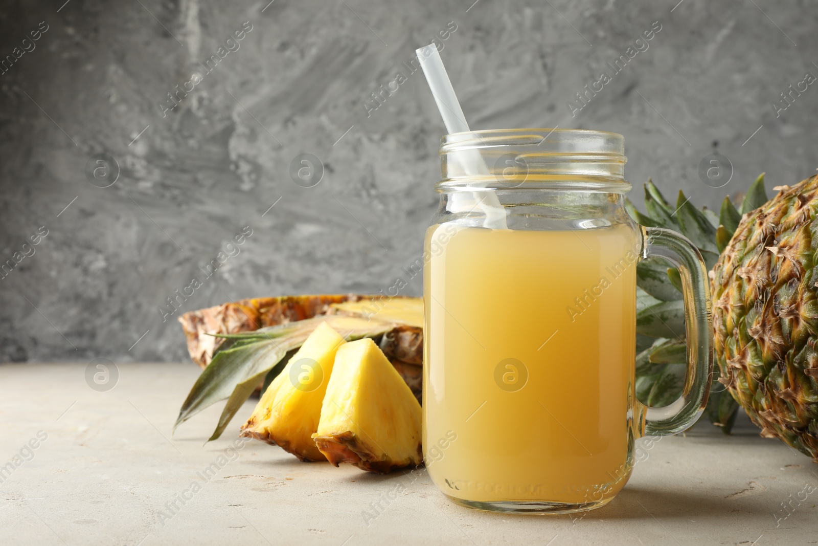 Photo of Tasty pineapple juice in mason jar and fresh fruits on grey textured table, closeup. Space for text