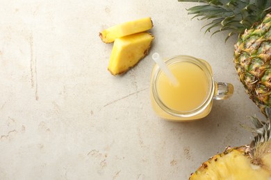 Photo of Tasty pineapple juice in mason jar and fresh fruits on grey textured table, flat lay. Space for text