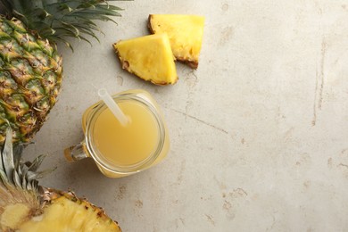 Photo of Tasty pineapple juice in mason jar and fresh fruits on grey textured table, flat lay. Space for text