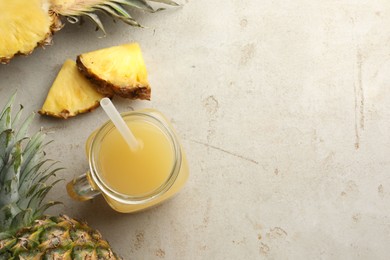 Photo of Tasty pineapple juice in mason jar and fresh fruits on grey textured table, flat lay. Space for text