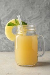 Photo of Tasty pineapple juice in mason jar, mint and slice of fresh fruit on grey textured table, closeup