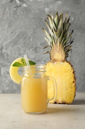 Photo of Tasty pineapple juice in mason jar, mint and slice of fresh fruit on grey textured table