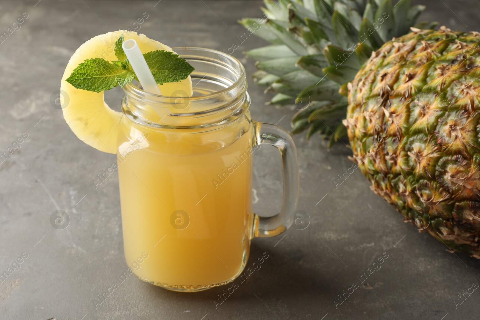 Photo of Tasty pineapple juice in mason jar, mint and fruit on grey textured table, closeup