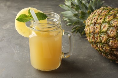 Photo of Tasty pineapple juice in mason jar, mint and fruit on grey textured table, closeup