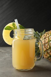 Photo of Tasty pineapple juice in mason jar, mint and fruit on grey textured table, closeup