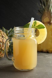 Photo of Tasty pineapple juice in mason jar, mint and fruits on grey textured table, closeup