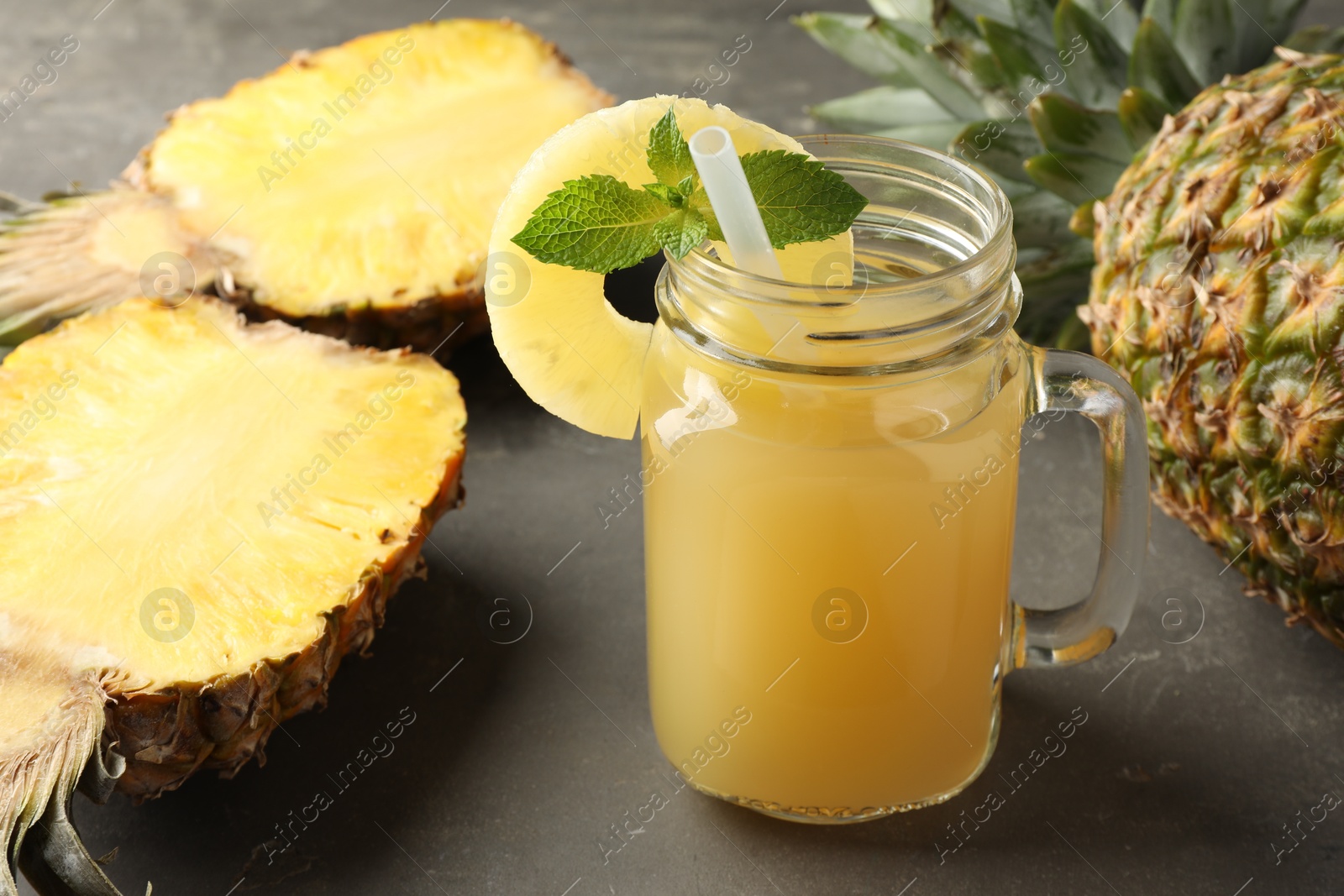 Photo of Tasty pineapple juice in mason jar, mint and fruits on grey textured table, closeup