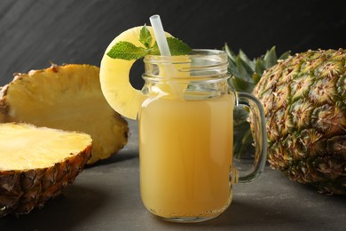 Photo of Tasty pineapple juice in mason jar, mint and fruits on grey textured table, closeup