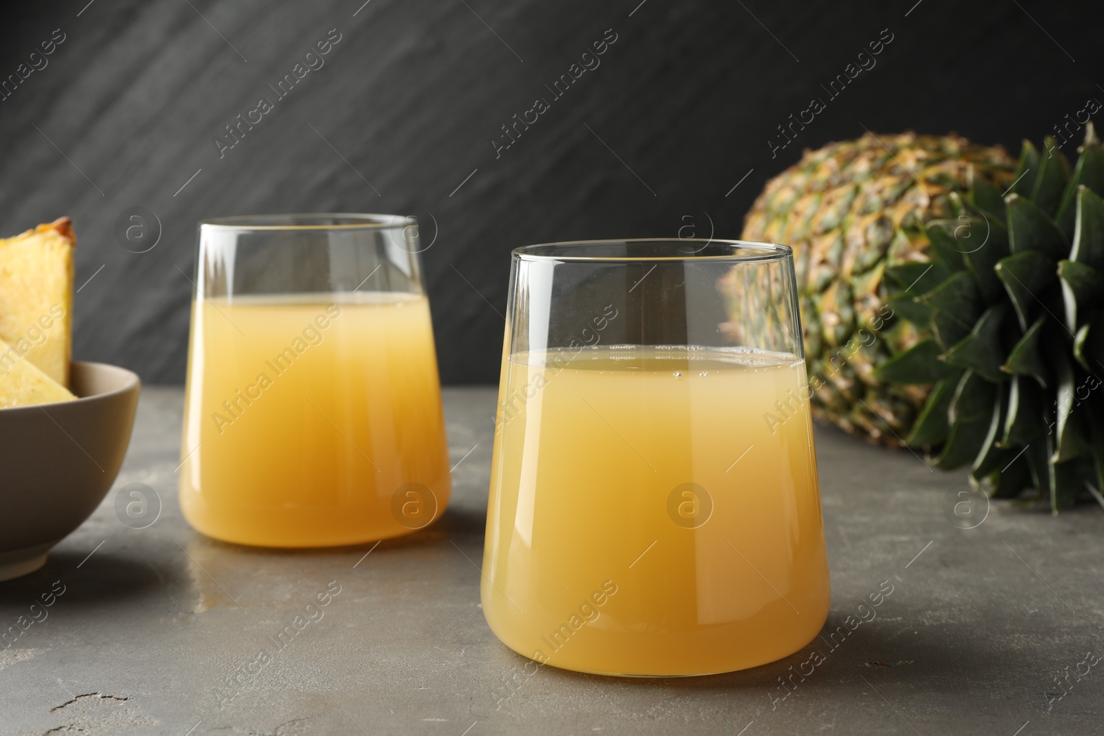 Photo of Tasty pineapple juice in glasses and fruits on grey textured table, closeup