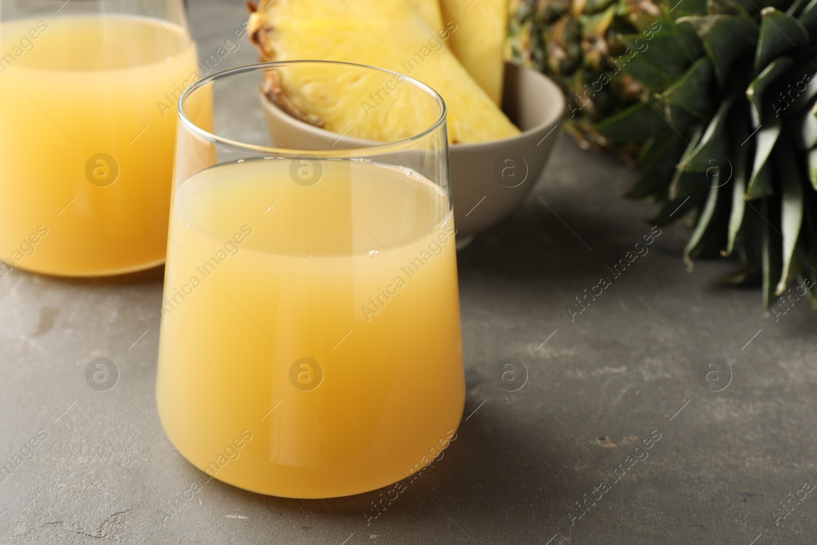 Photo of Tasty pineapple juice in glasses and fruits on grey textured table, closeup