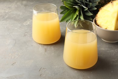 Photo of Tasty pineapple juice in glasses and fruits on grey textured table, closeup