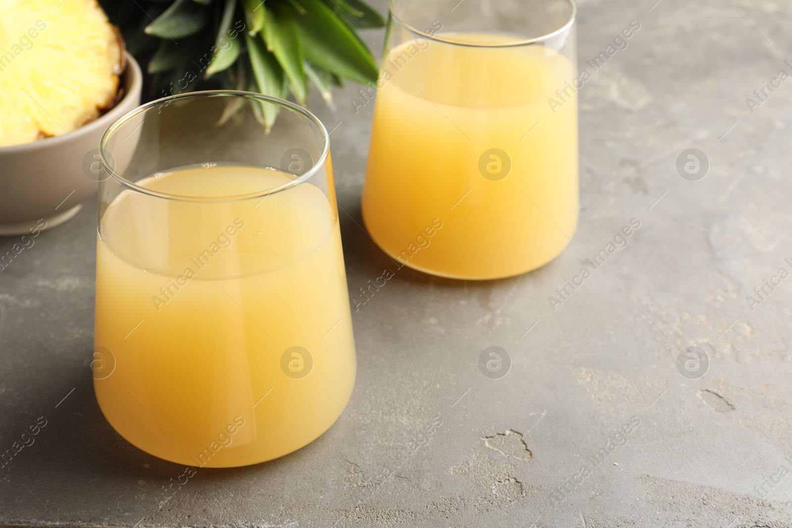 Photo of Tasty pineapple juice in glasses and fruits on grey textured table, closeup