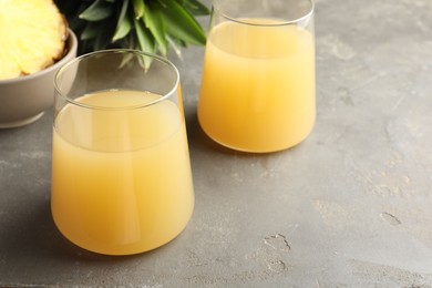 Photo of Tasty pineapple juice in glasses and fruits on grey textured table, closeup