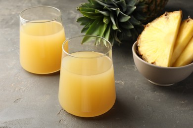 Photo of Tasty pineapple juice in glasses and fruits on grey textured table, closeup