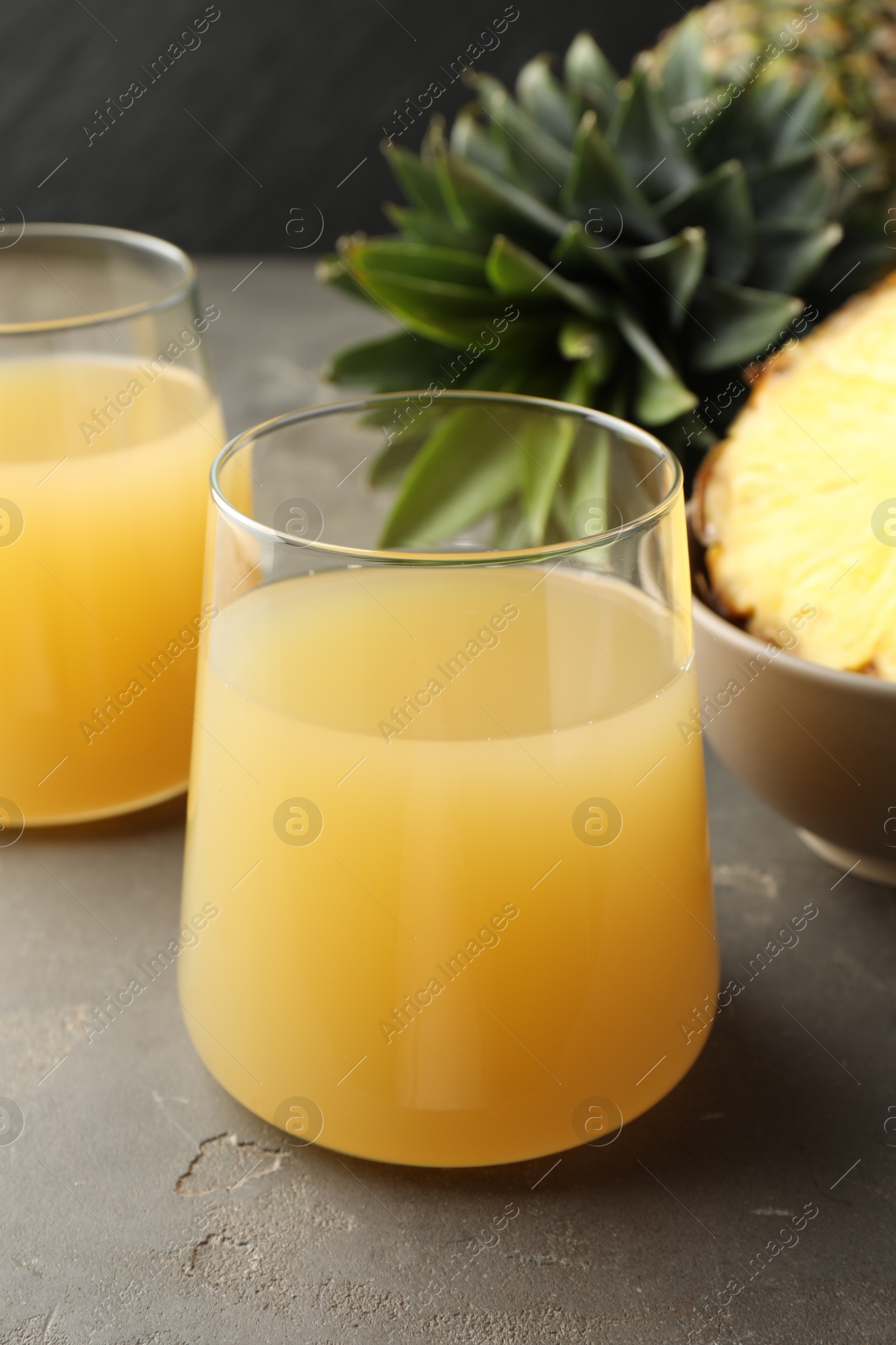 Photo of Tasty pineapple juice in glasses and fruits on grey textured table, closeup